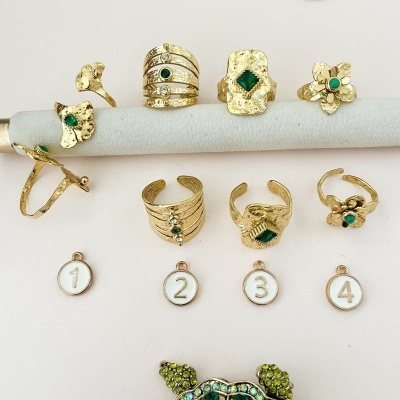 Anéis dourados com pedras verdes sobre suporte cinza e medalhas numeradas