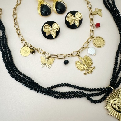 Conjunto de joias douradas e pretas com pendentes variados sobre fundo claro