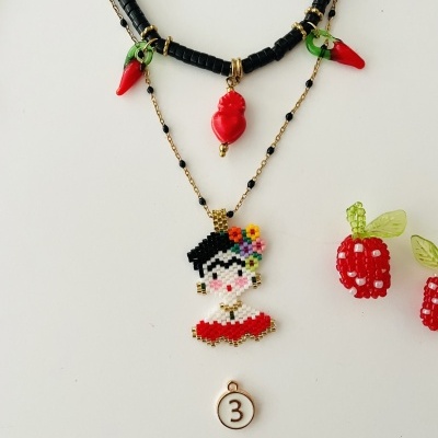 Conjunto de colares e brincos coloridos com pingentes de pimenta, coração, senhora bordada e framboesas, sobre superfície branca.