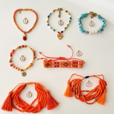 Sete pulseiras coloridas numeradas, com contas, tasséis e pingentes, dispostas sobre fundo branco.