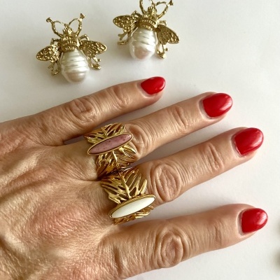 Anéis dourados com pedras ovais rosa e branca e brincos dourados de abelha com pérola