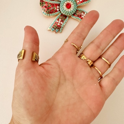 Mão com cinco anéis dourados e enfeite de parede floral colorido ao fundo