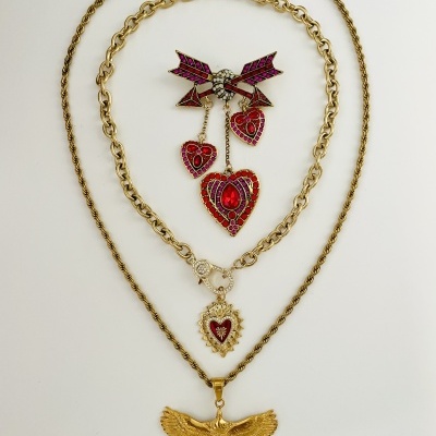 Jóias douradas com pendentes de águia, corações vermelhos e broche com pedras coloridas