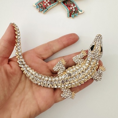Broche em forma de lagarto com pedras brilhantes segurado por mão, broche laço colorido no fundo branco