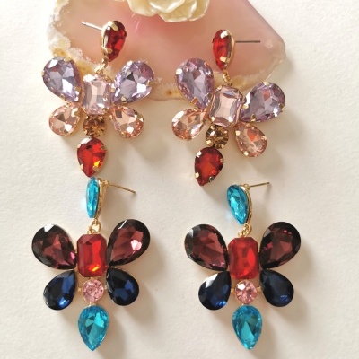 Brincos pendentes coloridos em forma de borboleta sobre superfície branca com pedra decorativa rosa