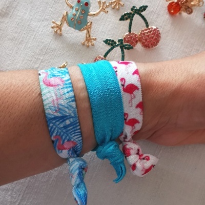 Pulseiras de tecido azuis e brancas com flamingos cor-de-rosa no pulso e brincos decorativos ao fundo