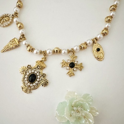 Colar com contas brancas e pendentes dourados variados sobre fundo branco com flor decorativa.