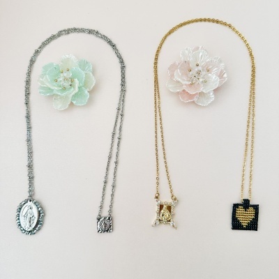 Dois colares com pingentes e flores artificiais num fundo claro