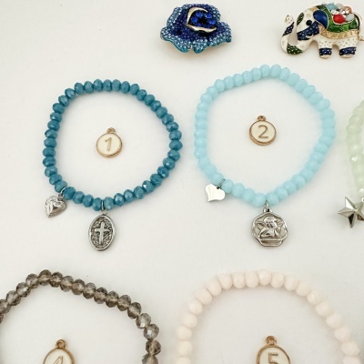 Pulseiras de contas facetadas em várias cores com pendentes metálicos e etiquetas numéricas.