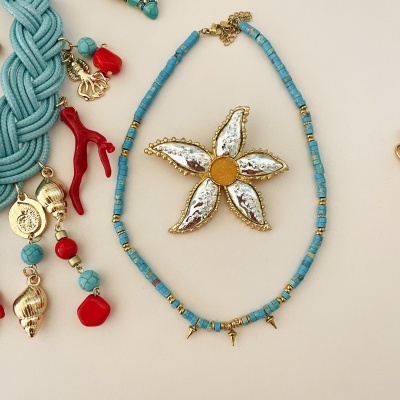 Colar com contas azuis e flor decorativa prateada e dourada num fundo claro