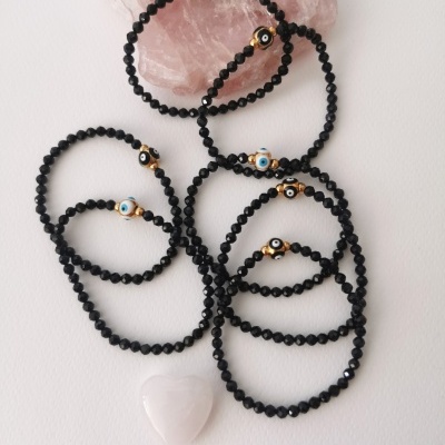 Pulseiras de contas pretas com contas de olho turco e detalhes dourados sobre pedra rosa
