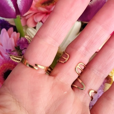 Mão com anéis dourados delicados e flores coloridas ao fundo