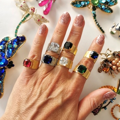 Mão com anéis de pedras coloridas e broches de insetos coloridos sobre fundo branco