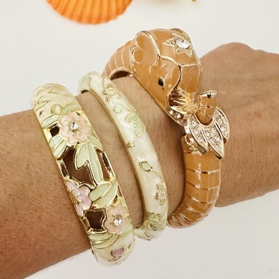 Pulseiras douradas com detalhes florais em esmalte e pulseira de cobra dourada com pedras
