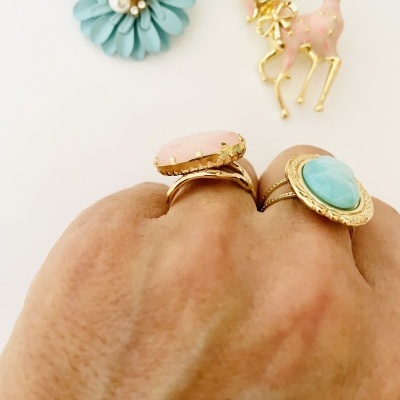 Anéis dourados com pedras rosa e azul e broches coloridos no fundo branco