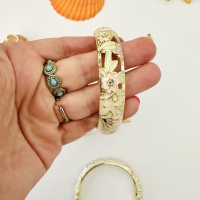 Pulseira dourada com flores esmaltadas em mão com anéis em fundo branco