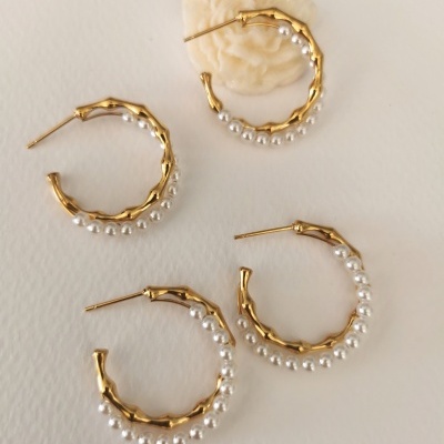 Quatro argolas douradas com pérolas brancas, sobre superfície branca e uma em suporte creme.