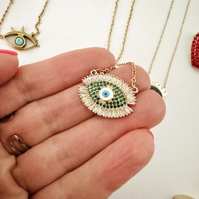 Colar em forma de olho com pedras verdes, brancas e azul claro em fundo branco.