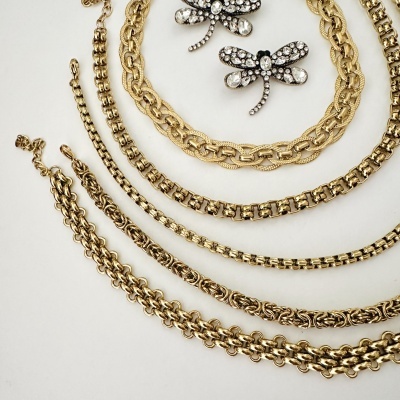 Colares dourados e broches de libélula com pedras brilhantes sobre fundo branco