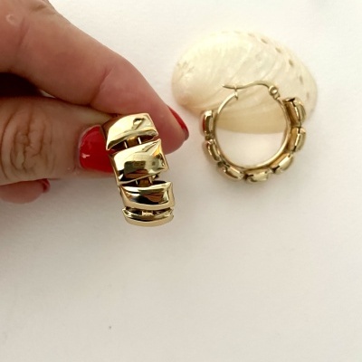 Brincos de argola dourados com padrão quadrado e mão com unhas vermelhas