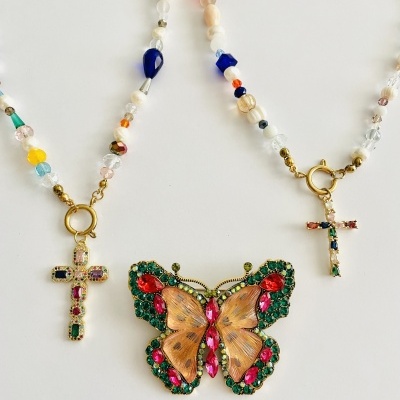 Colares com contas coloridas e pendentes em forma de cruz e borboleta com pedras coloridas.