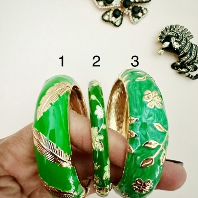 Três pulseiras verdes com detalhes dourados em forma de folhas e broches no fundo