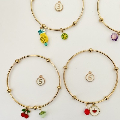 Quatro pulseiras douradas com pendentes coloridos e etiquetas numeradas