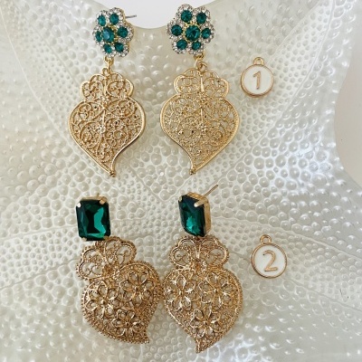 Dois pares de brincos dourados com pedras verdes sobre uma estrela-do-mar branca.