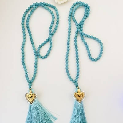 Dois colares de contas azuis com pendentes dourados e franjas azuis e prendedor de cabelo branco com detalhe dourado