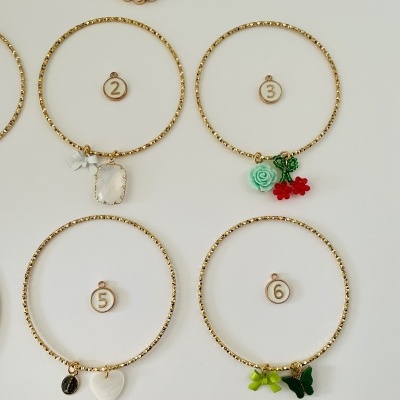 Quatro pulseiras douradas com diferentes pendentes coloridos sobre fundo branco, numeradas 2, 3, 5 e 6