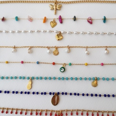 Braceletes ou tornozeleiras coloridas com pendentes e contas sobre fundo branco.