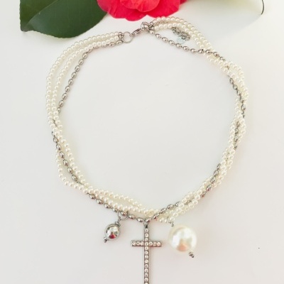 Colar de pérolas com cruz e dois pendentes sobre fundo branco com flor vermelha