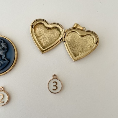 Medalhão dourado em forma de coração aberto com cinco anéis numerados