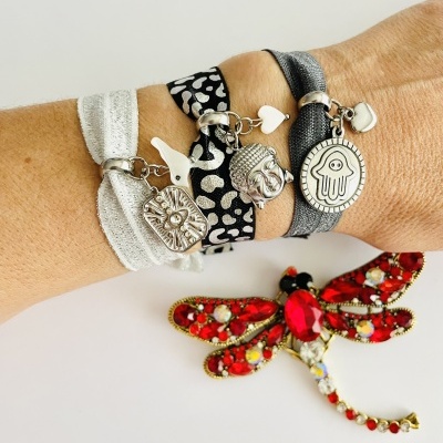 Pulseiras com pendentes metálicos e broche em forma de libélula vermelha sobre superfície branca