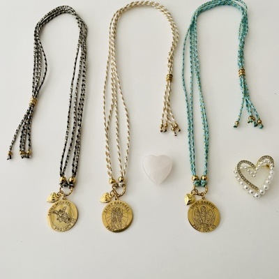 Três colares com medalhões dourados e adornos em forma de coração sobre superfície branca