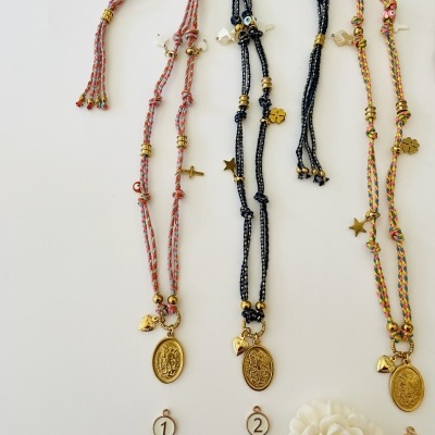 Três colares artesanais coloridos com pendentes dourados religiosos e etiquetas numeradas