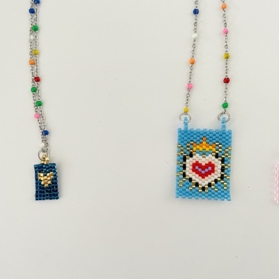 Dois colares com pendentes de contas coloridas, um com padrão de coração e outro com padrão amarelo sobre azul escuro.