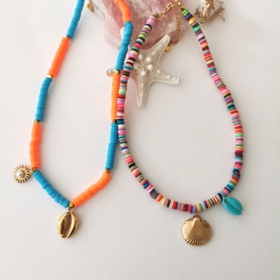 Dois colares coloridos com pendentes de conchas e elementos marinhos sobre fundo branco e pedra rosa