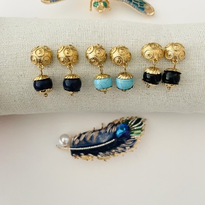 brincos dourados com bolas de cor azul escuro e turquesa e duas broches, uma de libélula azul e outra de pena azul com pérola