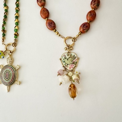 dois colares, um com pingente de tartaruga dourada colorida e outro com pingente de coração com pássaro e pedras