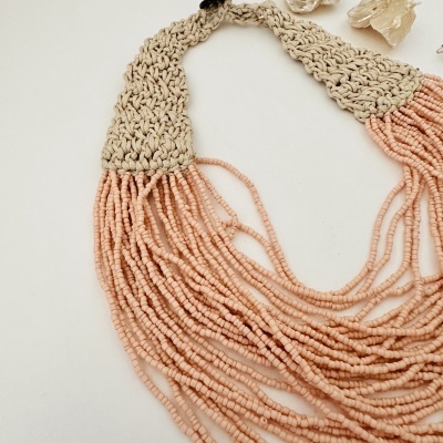 Colar artesanal bege com franjas cor-de-rosa claro e elementos decorativos neutros