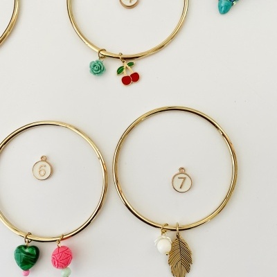 Três pulseiras douradas com pendentes coloridos e números 4, 6, 7 sobre fundo branco