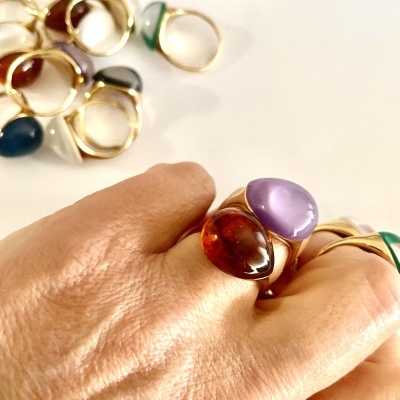 Anéis dourados com pedras coloridas numa mão e sobre superfície branca