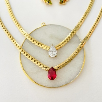 Colares dourados com pendentes em forma de gota e broche colorido ao fundo