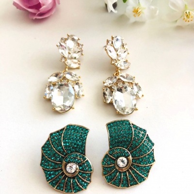 Dois pares de brincos com cristais transparentes e verdes sobre fundo branco com flores