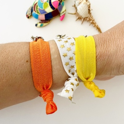 Pulseiras elásticas laranja, branca com estrelas douradas e amarelo usadas no pulso