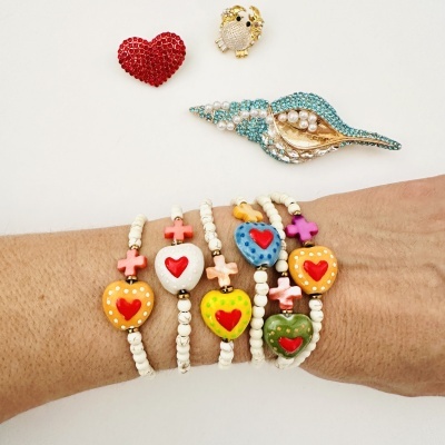 Pulseiras coloridas com corações vermelhos e cruzes e broches brilhantes em fundo branco