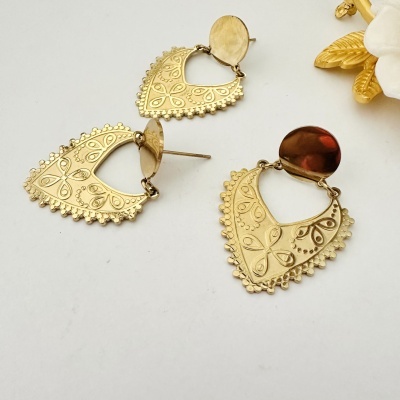 Brincos dourados com padrão floral e flor branca decorativa ao fundo