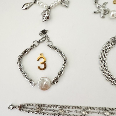 Três pulseiras prateadas com diferentes pendentes e pedras