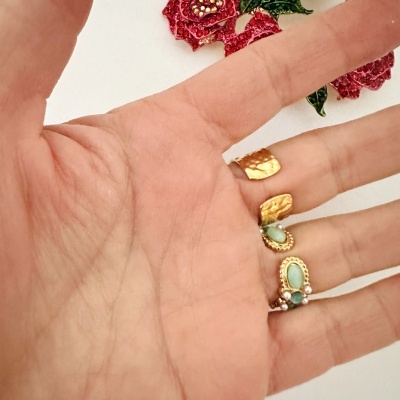 Mão com três anéis dourados e flor decorativa no fundo